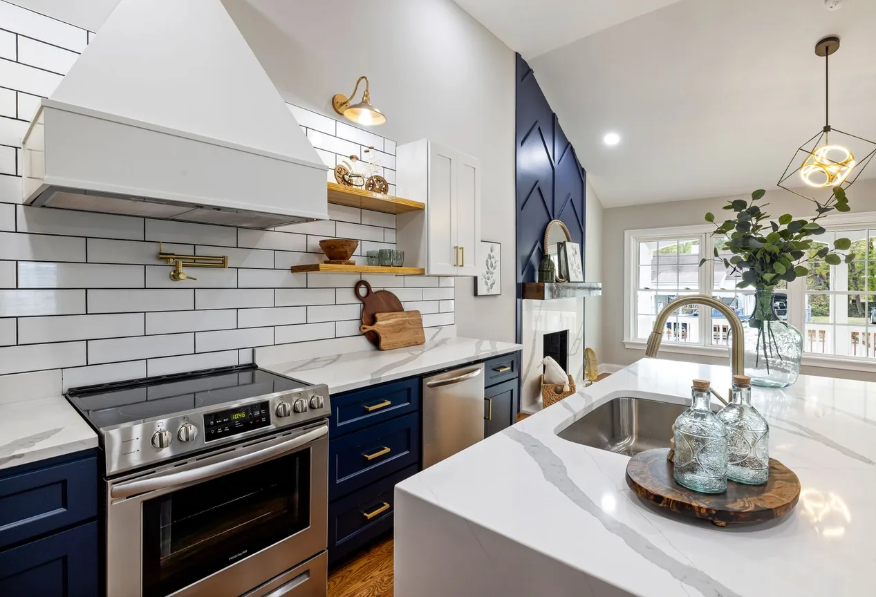 A kitchen with navy lower cabinets, white stone counters and brass fittings