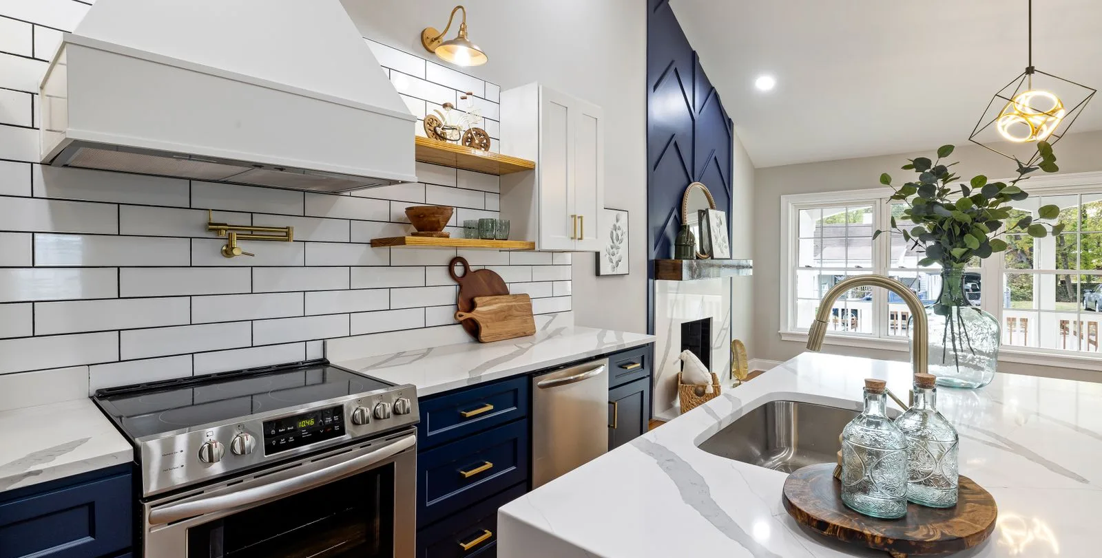 A kitchen with navy lower cabinets, white stone counters and brass fittings