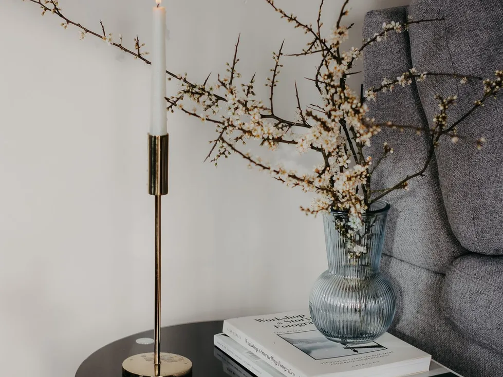 A side table with a brass candlestick, books and flowering branches