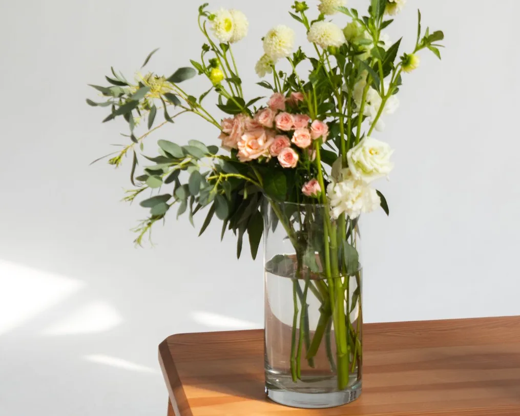 A vase of fresh flowers on a wooden side table in soft daylight