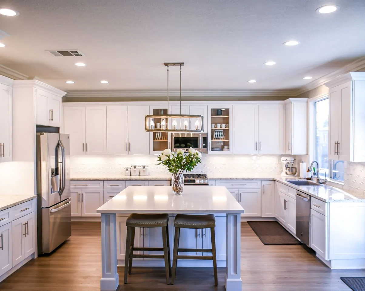 A white kitchen with a large island and a vase of white peonies